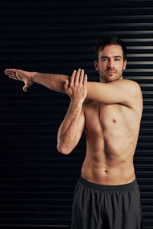 Dont forget to warm up. Studio portrait of a shirtless and well built man warming up against a dark...
