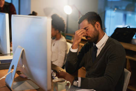 Feeling the pressure. Shot of a stressed out young businessman working late at the office with his colleagues.の写真素材