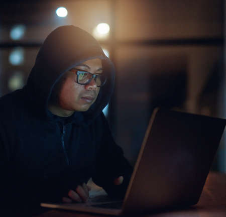 He can crack through any system. Shot of a hacker using a laptop in the dark.