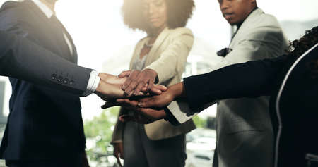 Working together for the benefit of all. Closeup shot of a group of unidentifiable businesspeople joining their hands in a huddle.の写真素材
