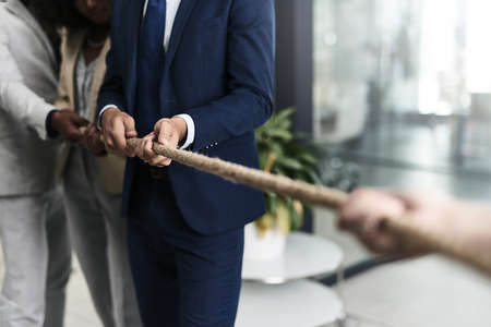 Teamwork can defeat any challenge. Closeup shot of a group of unrecognizable businesspeople pulling together on a rope in an office.の写真素材