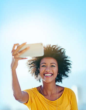 Selfies in the sunshine. Cropped shot of an attractive young woman taking selfies while standing...