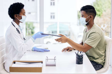 Please fill this out. Cropped shot of an attractive young female doctor handing a clipboard to a...