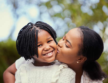 Having a mother means having a best friend for life. Shot of a young mother giving her daughter a kiss in nature.の写真素材