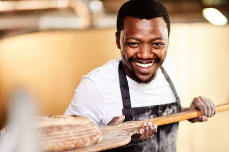 Freshly baked only for you. Cropped shot of a male baker removing freshly baked bread from the oven.の写真素材