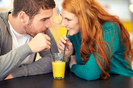 Juicy romance. Cropped shot of a happy young couple sharing a glass of juice on a date at a cafe.の写真素材