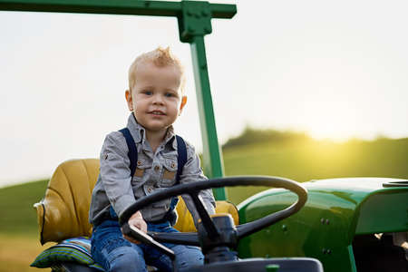 Growing up with good old fashioned farming values. Portrait of an adorable little boy riding a tractor on a farm.の写真素材