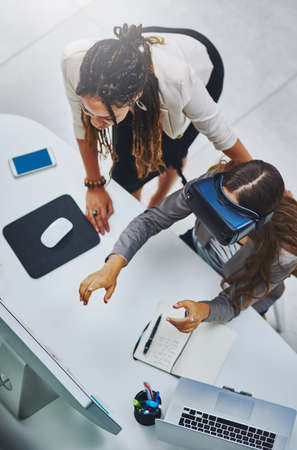Submerged in business. High angle shot of a young businesswoman using a VR headset while being...