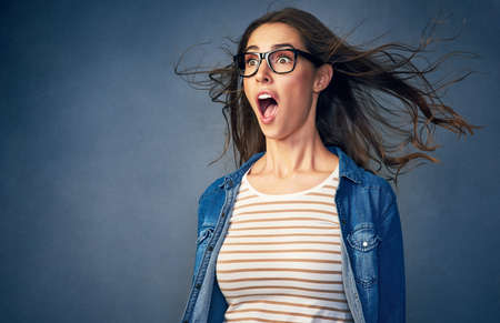 Surprise. Shot of a happy young woman with air being blown in her face in studio.