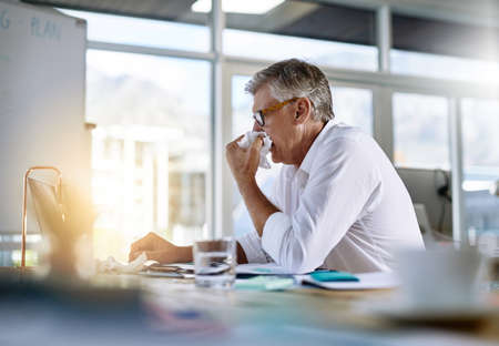Its difficult working when you sick. Shot of a mature businessman suffering with the flu in the...
