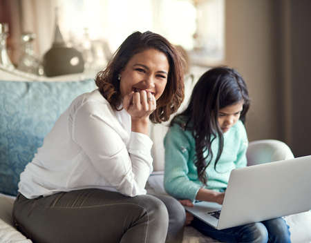 Supervised internet sessions because online safety starts at home. Portrait of a happy woman sitting next to her daughter while she uses a laptop at home.の写真素材