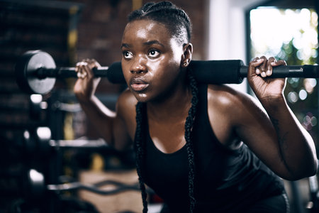 Fully focused. Full length shot of an attractive young female athlete lifting weights in the gym.の写真素材