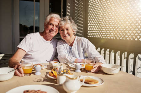 We still start our mornings together. Shot of a happy senior couple having a leisurely breakfast on the patio at home.の写真素材