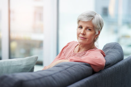 Always choose your own peace before anything else. Portrait of a cheerful mature woman relaxing on her sofa at home.の写真素材