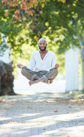 Yogas got him floating. Full length shot of a handsome young man levitating while meditating outside at the park.の写真素材