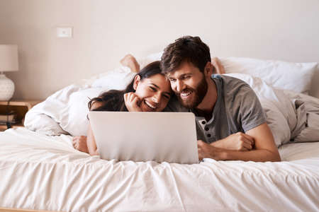 Some people just have that special connection. Shot of a happy young couple using a laptop while relaxing on the bed at home.の写真素材