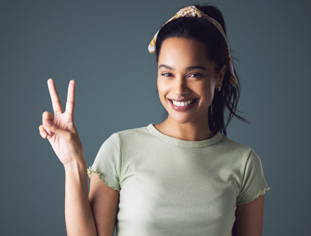 What do I want I want peace. Studio shot of a young woman showing the peace sign while standing against a grey background.の写真素材