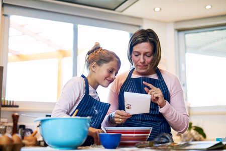 Lets see what the recipe says.... Shot of a mother and her little daughter baking together at home.の写真素材