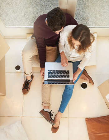 Finding something special for their new home. High angle shot of a young couple using a laptop while moving into a new home.の写真素材