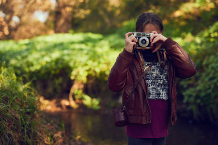 Looking at the world through a different lens. Shot of a young girl taking pictures with a vintage camera outdoors.の写真素材