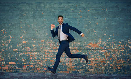 Eager to succeed. Portrait of a young corporate businessman jumping midair against a brick wall.の写真素材