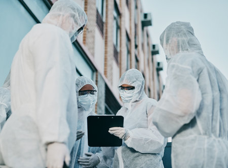 Teamwork makes infection control work. Shot of a group of healthcare workers wearing hazmat suits working together during an outbreak in the city.の写真素材