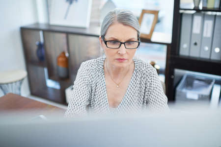Focused on her deadlines. Shot of a mature businesswoman working on a computer in an office.の写真素材