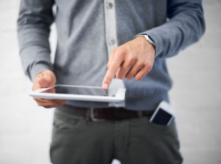 Managing his diary online. Cropped image of a young man working on his digital tablet.の写真素材