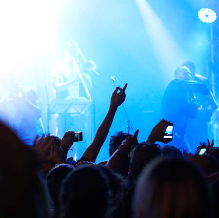 Making the memories last. Rearview of an audience with hands raised at a music festival.の写真素材