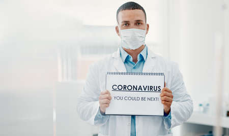 Were all at risk. Shot of a scientist holding a sign with CORONAVIRUS-YOU COULD BE NEXT on it in a laboratory.の写真素材