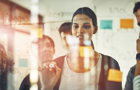 I have great minds behind me. Cropped shot of a group of young designers using sticky notes during a...