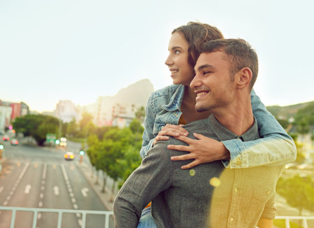 Young urban love. Shot of a happy young couple enjoying a piggyback ride in the city.の写真素材