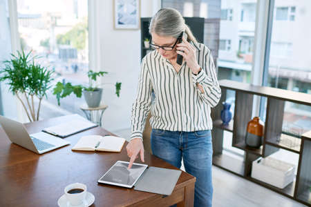 Upholding a solid connection to success. Shot of a mature businesswoman talking on a cellphone while using a digital tablet in an office.の写真素材
