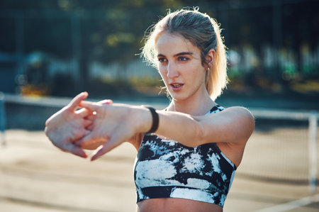 Prepping with some stretches. Shot of a sporty young woman stretching her arms while exercising on a tennis court.の写真素材