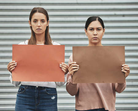 Dont be afraid to be different. Cropped portrait of two attractive young women holding signs while taking part in a political rally.の写真素材