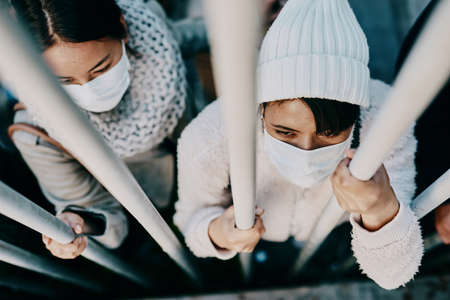 Prisoners of a viral war. Shot of a group of young people wearing masks while stuck behind a gate in a foreign city.の写真素材