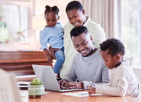Family gives you the roots to stand tall and strong. Shot of a happy young family huddled together while looking at a laptop at home.の写真素材