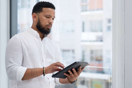 Staying efficient while handling tasks. Shot of a young businessman using a digital tablet in an office.の写真素材