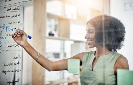Planning and execution. Cropped shot of an attractive young businesswoman working on a glass wipe...
