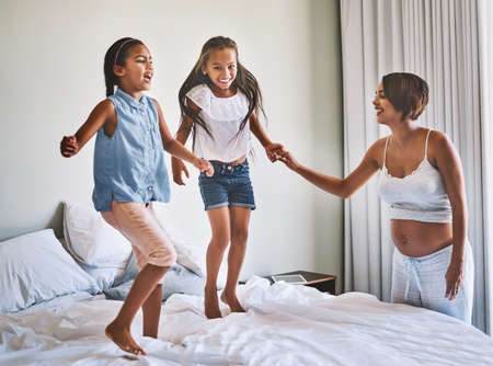 Jumping around. Shot of a cheerful young family jumping around on a bed together at home during the day.の写真素材
