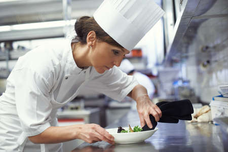 Chefs at work. Shot of a chef putting the final touches on a dinner plate in a professional kitchen.の写真素材