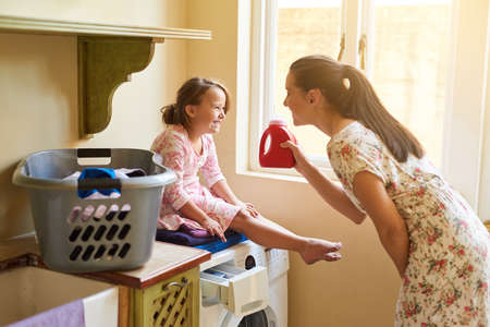 This is what keeps our clothes smelling so fresh. Shot of a mother and daughter doing laundry together at home.の写真素材