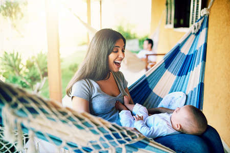 Such a good boy. Shot of a cheerful young mother relaxing on a hammock with her infant son outside at home during the day.の写真素材