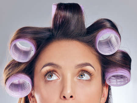 Please be perfect waves. Cropped shot of an attractive young woman standing alone in the studio and posing with rollers in her hair.の写真素材