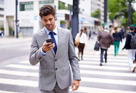 The modern multitasking man. A cropped shot of a handsome young businessman texting while walking in the city.の写真素材