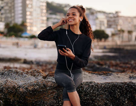 Raising my vibration through frequency music. Shot of an attractive young woman sitting alone on the beach after yoga and listening to music.の写真素材