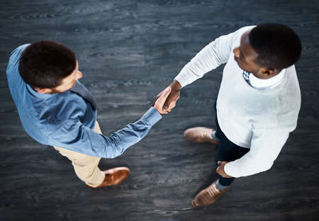 Lets take over the business world. High angle shot of two businessmen shaking hands while standing in an office.の写真素材
