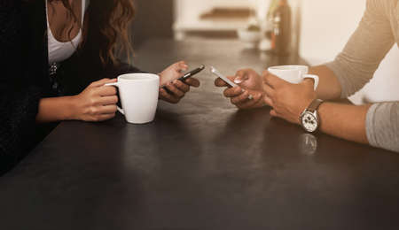 Whats better than coffee and wifi. Cropped shot of a young couple using their mobile phones and...