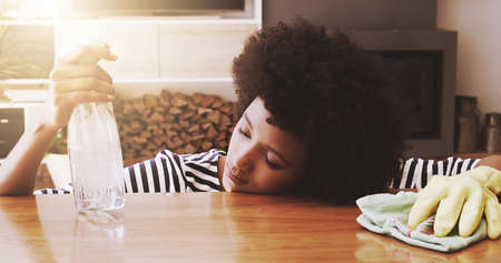 Shes been cleaning the whole day. Shot of a tired young woman resting her head on a table after trying to clean it with cleaning equipment at home during the day.の写真素材