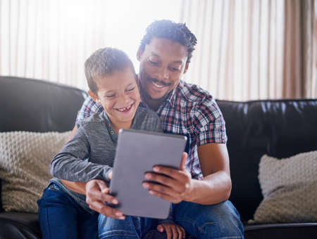 Lets watch that again Dad. Cropped shot of a father and son using a digital tablet at home.の写真素材